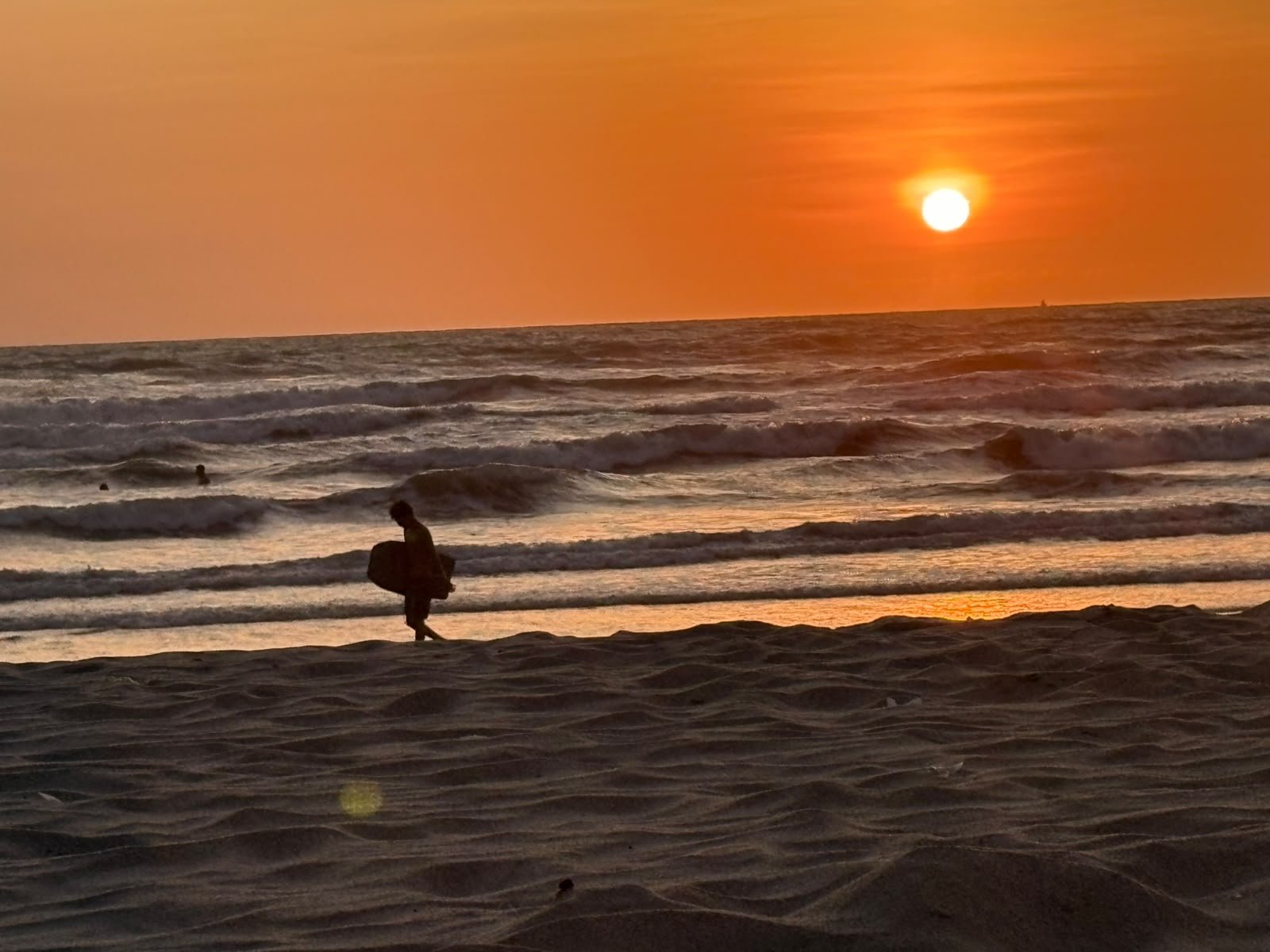 Silueta de un surfista caminando por la orilla al atardecer